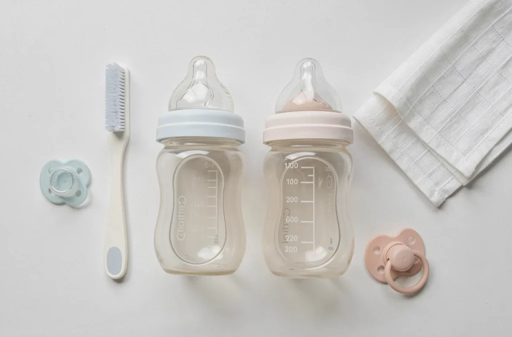 Comparatif de deux biberons bébé avec accessoires posés sur un plan de travail blanc